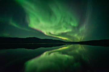 Aurora borealis seen in northern Canada Yukon Territory during fall with stunning green reflection band in the Yukon River below wilderness sky background, wallpaper, desktop.