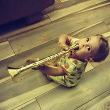 Portrait Of Cute Girl Playing Trumpet On Parquet Floor At Home