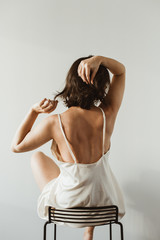 Young beautiful woman in silk underwear sitting on black stool on white background. Sexy fashion concept.