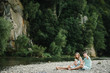 © Serhii - Family playing stones near water. Mom, dad hugging daughter sitting on beach near lake. The concept of summer holiday. Mother's, father's, baby's day. Spending time together. Family look.