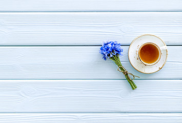 Wall Mural - Summer tea party. Cup near cornflowers bouquet on blue wooden background top-down copy space