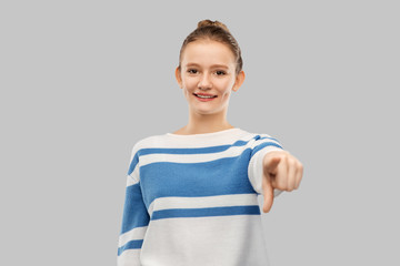 gesture and people concept - smiling teenage girl in pullover pointing finger to camera over grey background