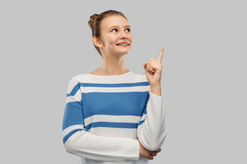 idea and people concept - smiling teenage girl in pullover pointing finger up over grey background