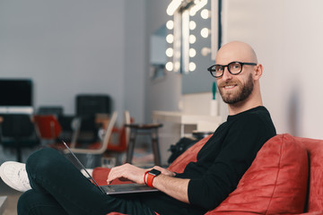 Wall Mural - Modern young caucasian man with beard and glasses relaxing while surfing internet on laptop pc