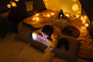 Wall Mural - little 11 year old girl using laptop under her home-made tent inside the living room.