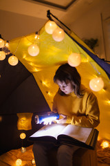 Wall Mural - young female child reading encyclopedia in a home made livingroom tent with light balls.