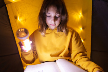 Wall Mural - young female child reading encyclopedia in a home made livingroom tent with light balls.