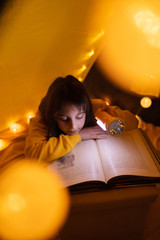 Wall Mural - young female child reading encyclopedia in a home made livingroom tent with light balls.