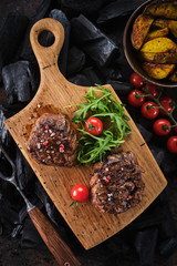 Grilled fillet steaks on wooden cutting board. Succulent thick juicy portions of grilled fillet steak served with tomatoes and roast potatoes on an old wooden board.