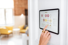 Controlling Home With A Digital Touch Screen Panel Installed On The Wall In The Living Room. Concept Of A Smart Home And Mobile Application For Managing Smart Devices At Home