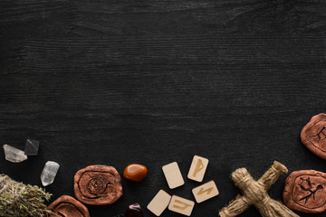 Top view of shamanic amulets, doll and runes on black wooden background