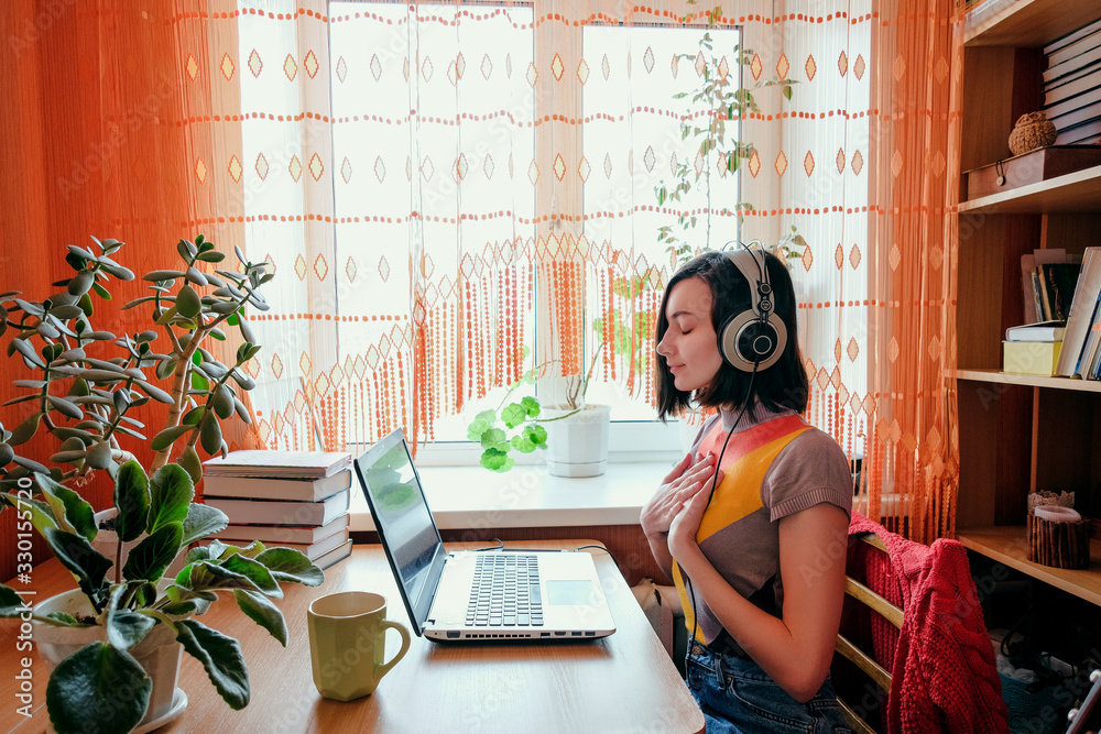 Female in headphones sits at front of laptop and breathing. Online audio meditation concept. - obrazy, fototapety, plakaty 
