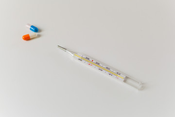 Thermometer and two capsules of orange and blue on a white table