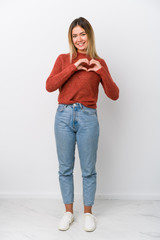 Wall Mural - Full body young caucasian woman smiling and showing a heart shape with hands.