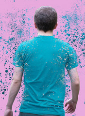 Back side of a pale skinned man with short brown curly hair wearing a blue shirt dispersing off of his body into small particles floating around him in front of a bright pink purple pastel background