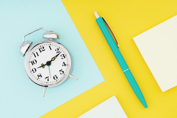 Metal vintage alarm clock with office pen on colorful paper background. Work and planning time flat lay concept