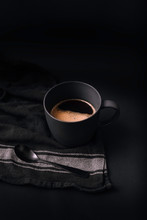 Photograph Of Black Coffee Cup With Coffee Foam And Black Spoon, On Black And White Cloth. All In Black Background.