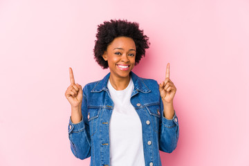 Wall Mural - Young african american woman against a pink backgroound isolated indicates with both fore fingers up showing a blank space.