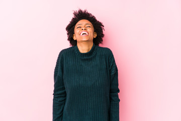 Wall Mural - Middle aged african american woman against a pink background isolated laughs and closes eyes, feels relaxed and happy.