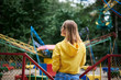 canvas print picture - Young blond woman, wearing yellow hoody and blue jeans, spending time in amusement theme park in summer. Three-quarter portrait from back of girl, looking at colorful ferris wheel. Sunday leisure