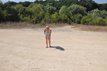 A Girl In Shorts And A Hat Points To Something In The Sand In Front Of Her