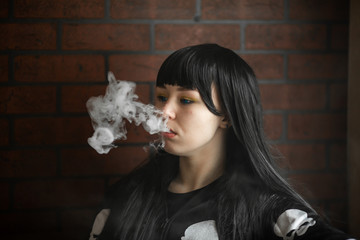 Wall Mural - Vaping teenager. Young pretty white caucasian teenage brunette girl with blue eyes and problem skin smoking an electronic cigarette indoors. Deadly bad habit. Vape activity.