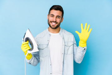 Wall Mural - Portrait of young man ironing isolated smiling cheerful showing number five with fingers.