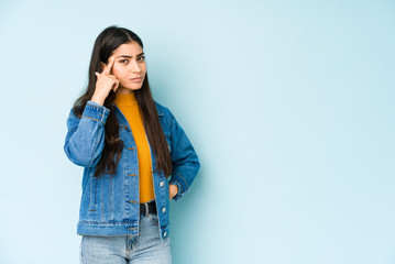 Wall Mural - Young indian woman isolated on blue background pointing temple with finger, thinking, focused on a task.