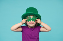 Funny Little Child Girl In Green Patricks Hat With Clover Glasses On Color Background. St. Patricks Day Celebration. Advertising Space