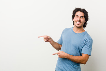 Wall Mural - Young handsome man against a white background excited pointing with forefingers away.