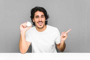 Wall Mural - Young man holding a moisturizer smiling cheerfully pointing with forefinger away.