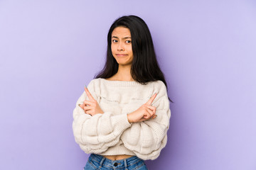 Young chinese  woman isolated on a purple background points sideways, is trying to choose between two options.