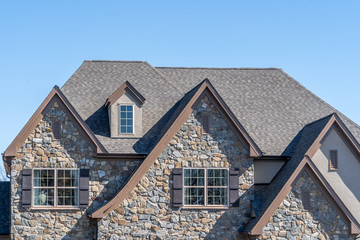 Double gable with dark stone veneer siding,  with triangle shape peaks, on a pitched roof attic at an American single family home neighborhood USA, double sash windows w/ matching dark shutters