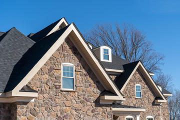 Wall Mural - Pointed  gable roofs with attic windows on a house covered with manufactured veneer stone blue sky background