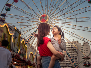 Wall Mural - happy asia mother and daughter have fun in amusement carnival park with farris wheel and carousel background