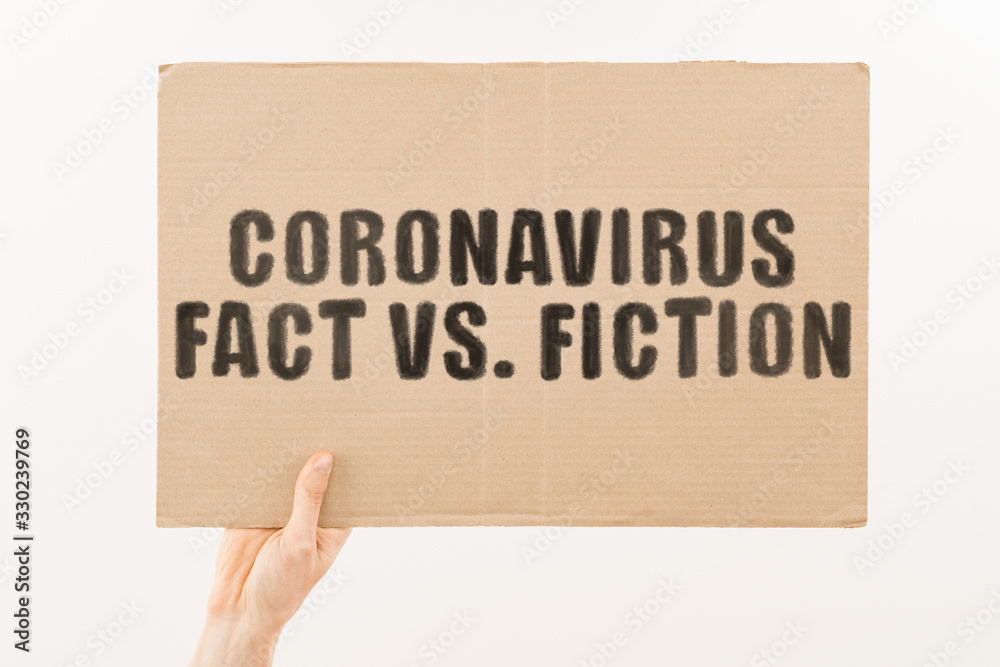The phrase " Coronavirus fact vs. fiction " on a banner in hand. Human holds a cardboard with an inscription. Outbreak. Quarantine. Infection. Pandemic. Global epidemic. COVID-2019 - obrazy, fototapety, plakaty 