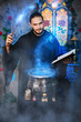 The mage is cooking a potion. A male wizard in a black mantle with a magic wand and a book. He casts a spell over the witch's cauldron. Guy in an old castle with luminous magic