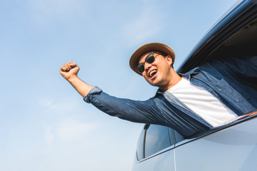 An Asian man is enjoying his trip. He stretches out of the car window to make him look happy.