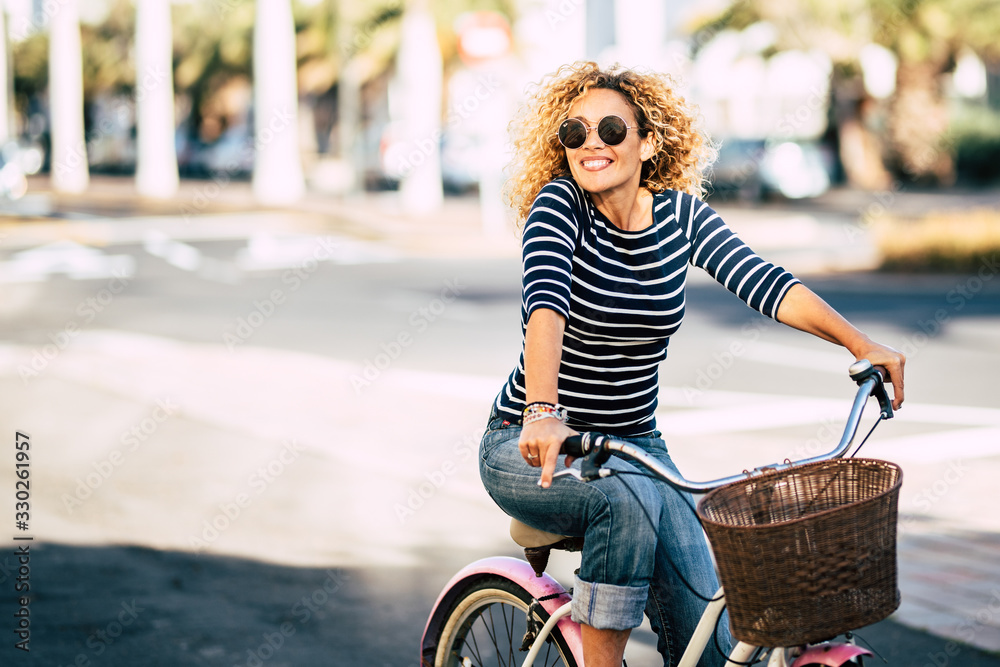 Beautiful and cheerful adult young woman enjoy bike ride in sunny urban outdoor leisure activity in the city - happy people portrait - trendy female outside having fun - obrazy, fototapety, plakaty 