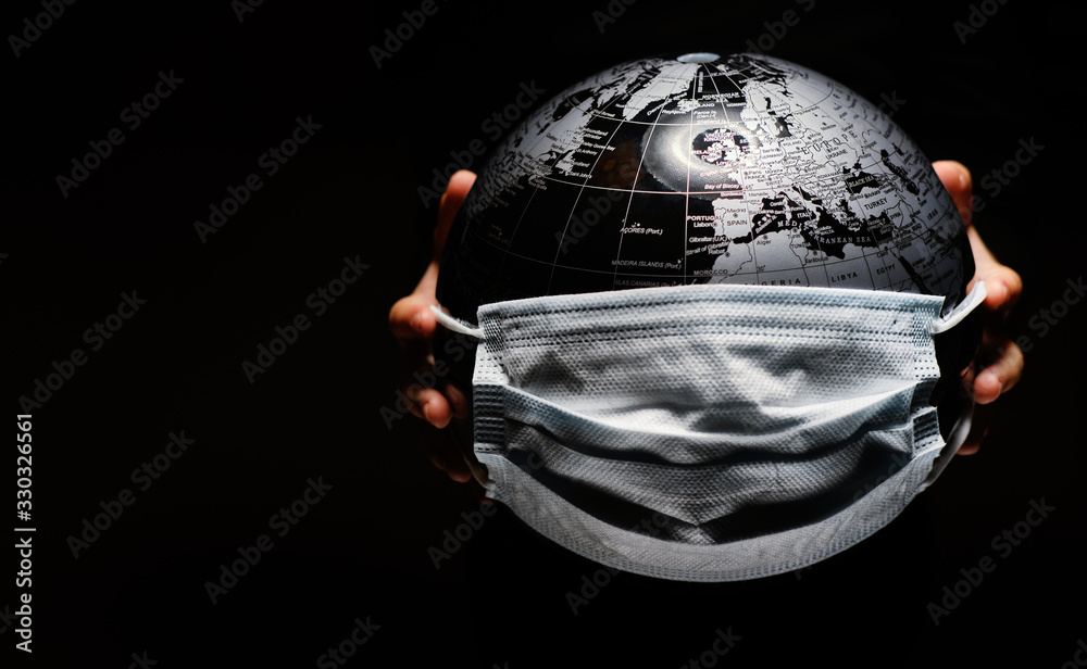 Hands of little child holding globe sphere, planet map covered with medical protective mask isolated on black background. Concept of COVID-19 pandemic infection - obrazy, fototapety, plakaty 
