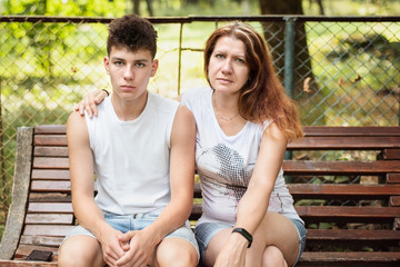 Serious teenager boy and his mother sit on a bench and calm down after a serious conversation, concept of relationship during adolescence