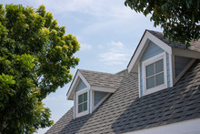 Roof Shingles With Garret House On Top Of The House Among A Lot Of Trees. Dark Asphalt Tiles On The Roof Background