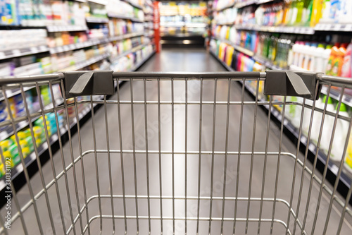 Cuadros en Lienzo Shopping trolley cart moving in supermarket with motion blur aisle background