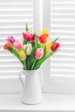 Bouquet With Multicolored Tulips On A Window With Wooden Blinds On A Light Background