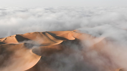 Aerial view of a massive sand dune surrounded by winter morning fog cloud in Empty Quarter. Liwa desert, Abu Dhabi, United Arab Emirates.