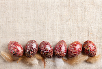 Traditional Ukrainian Pysanka placed in line with feathers on linen cloth background. Decorated Easter eggs, traditional for Eastern Europe culture.