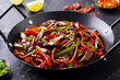Beef and vegetables stir fry in a pan. Dark background. Close up.