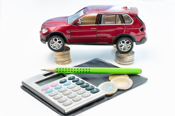 A red car (collectible toy) is placed on 1 and 2 euro coins and 50 cents. In front there is a calendar and a green pencil. The car has a broken traffic light and damages.