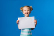baby girl holding a white sheet.Cute little girl with a white sheet of paper.blue background.space for text.A little girl holds an empty piece of paper