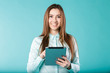 © Elizaveta - She always connected. Woman using digital tablet computer happy isolated on turquoise background. Portrait young caucasian woman worker, teacher, mentoring in shirt office style with tablet in hand